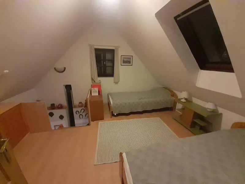 Tágas tetőtéri szoba két ággyal és ülőgarnitúrával